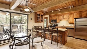 A modern kitchen with wooden cabinets, stainless steel appliances, and a glass dining area with metal chairs. - Chateau Eau Claire Unit 17 | Serene Condo Overlooking the River with Many Upgrades (Aspen)