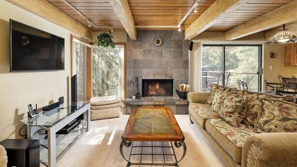 A cozy living room with a stone fireplace, wooden ceiling beams, and a comfortable sofa. - Chateau Eau Claire Unit 17 | Serene Condo Overlooking the River with Many Upgrades (Aspen)