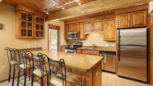 A kitchen with wooden cabinets, a stainless steel refrigerator, a microwave, and a granite countertop. - Chateau Eau Claire Unit 17 | Serene Condo Overlooking the River with Many Upgrades (Aspen)