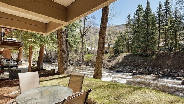 An outdoor patio with a round table and chairs, overlooking a flowing stream and surrounded by trees. - Chateau Eau Claire Unit 8 | Riverfront Condo, Walking Distance to Town (Aspen)