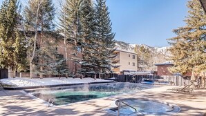 A pool area with a hot tub, surrounded by trees and a mountain backdrop. - Chateau Eau Claire Unit 8 | Riverfront Condo, Walking Distance to Town (Aspen)