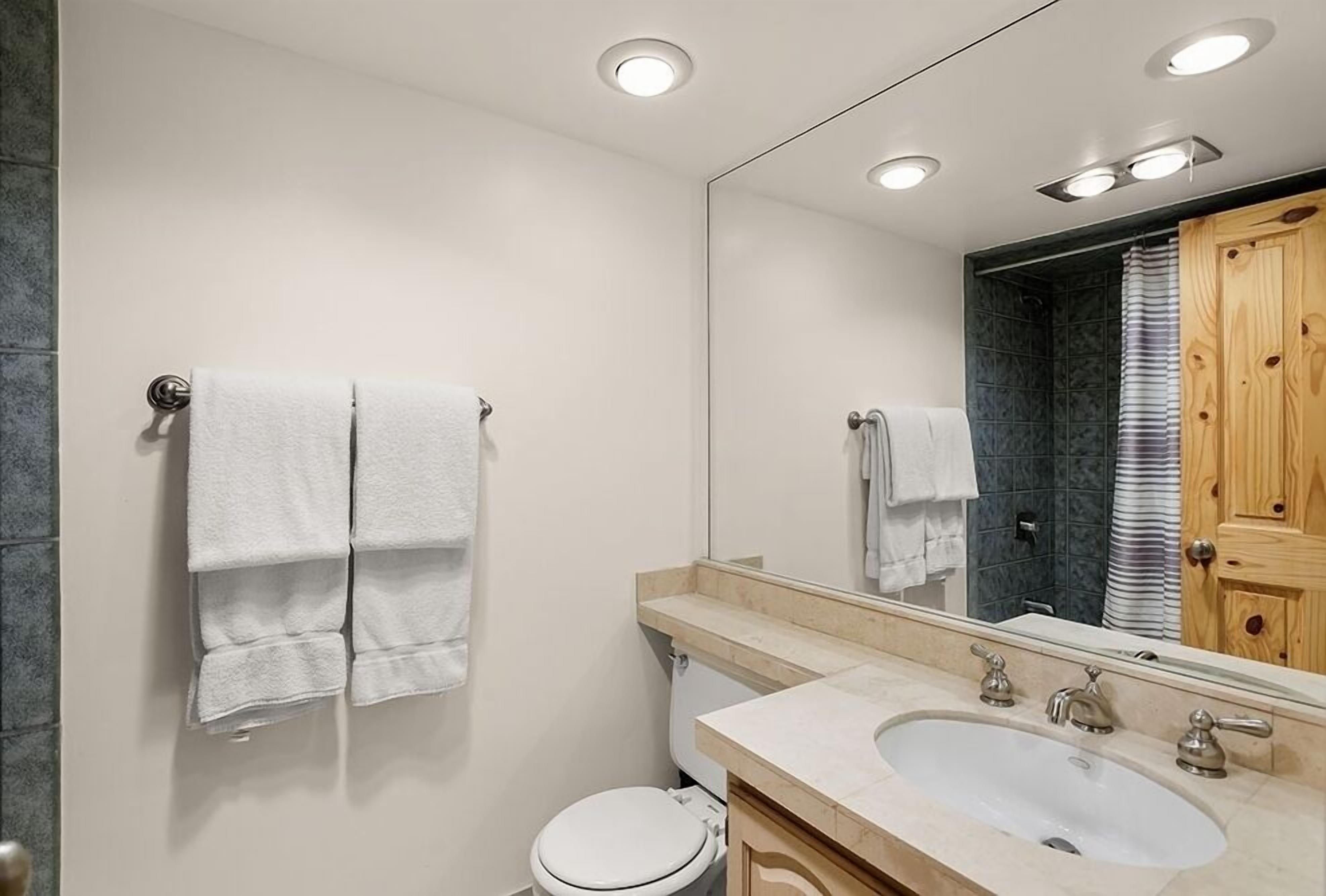 A modern bathroom with a white toilet, a sink with a mirror above it, and two towels hanging on a towel rack.
