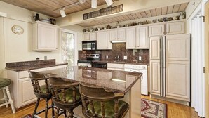 Una cocina con armarios blancos, encimera de granito y techo de madera.