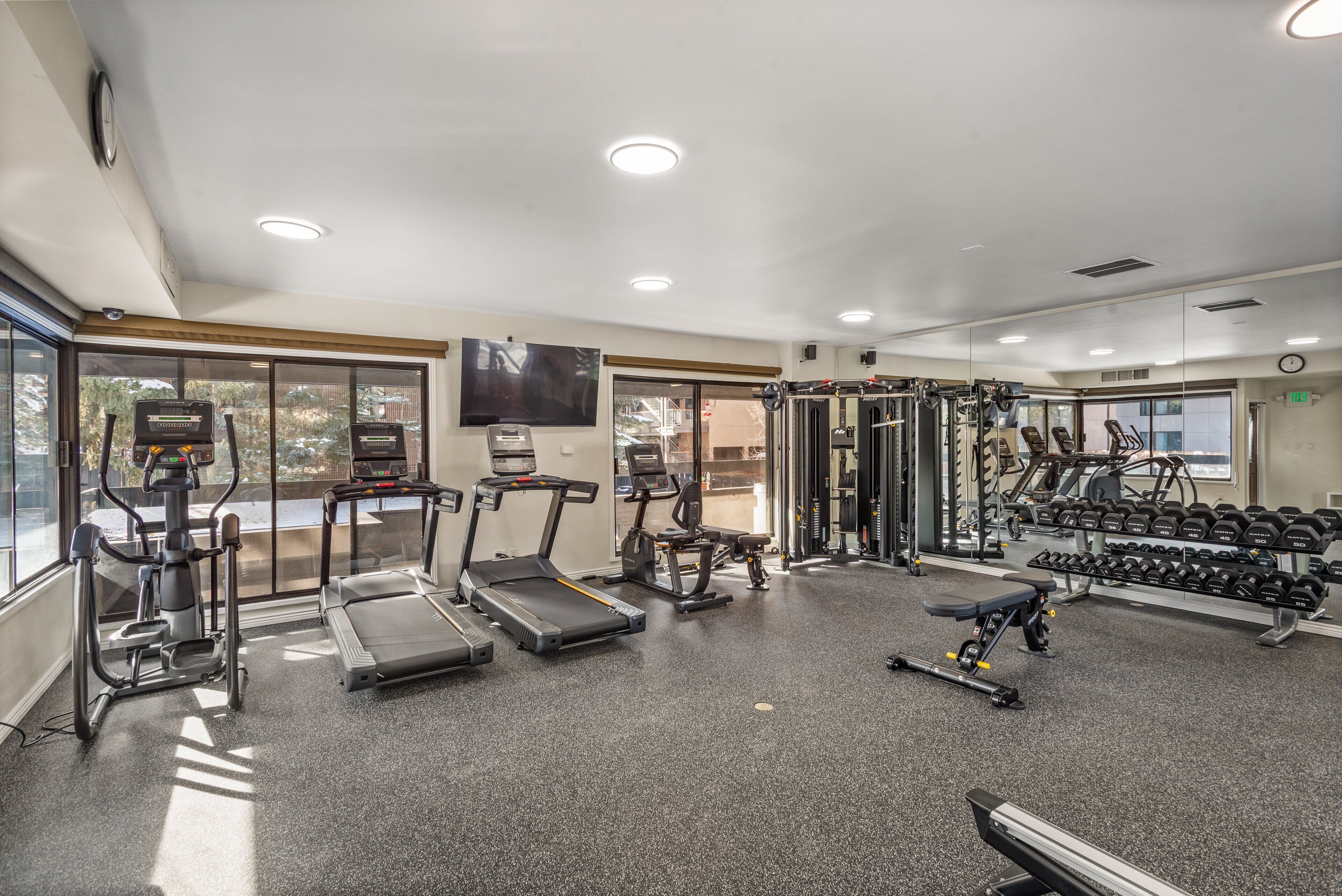 Une salle de sport équipée de tapis de course, de vélos elliptiques, d’un banc de musculation et de poids libres.