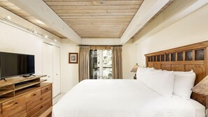 Ein Schlafzimmer mit einem hölzernen Bett, einem Fernseher auf einer Holzkommode und einem Fenster mit Vorhängen.