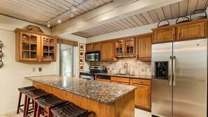 Eine Küche mit Holzausstattung, einem Edelstahlkühlschrank, einer Arbeitsplatte aus Granit und einer Bar-Ecke.