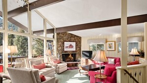 Un vaste salon doté d’une cheminée en pierre, de grandes fenêtres et d’un coin salon confortable avec un canapé rose et des fauteuils.