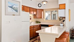 Une cuisine avec des meubles de rangement en bois, un îlot central blanc et une horloge au mur.