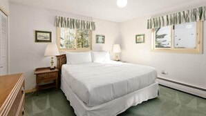 Une chambre à coucher avec un grand lit, deux tables de chevet avec des lampes, une commode et des tableaux encadrés accrochés aux murs.