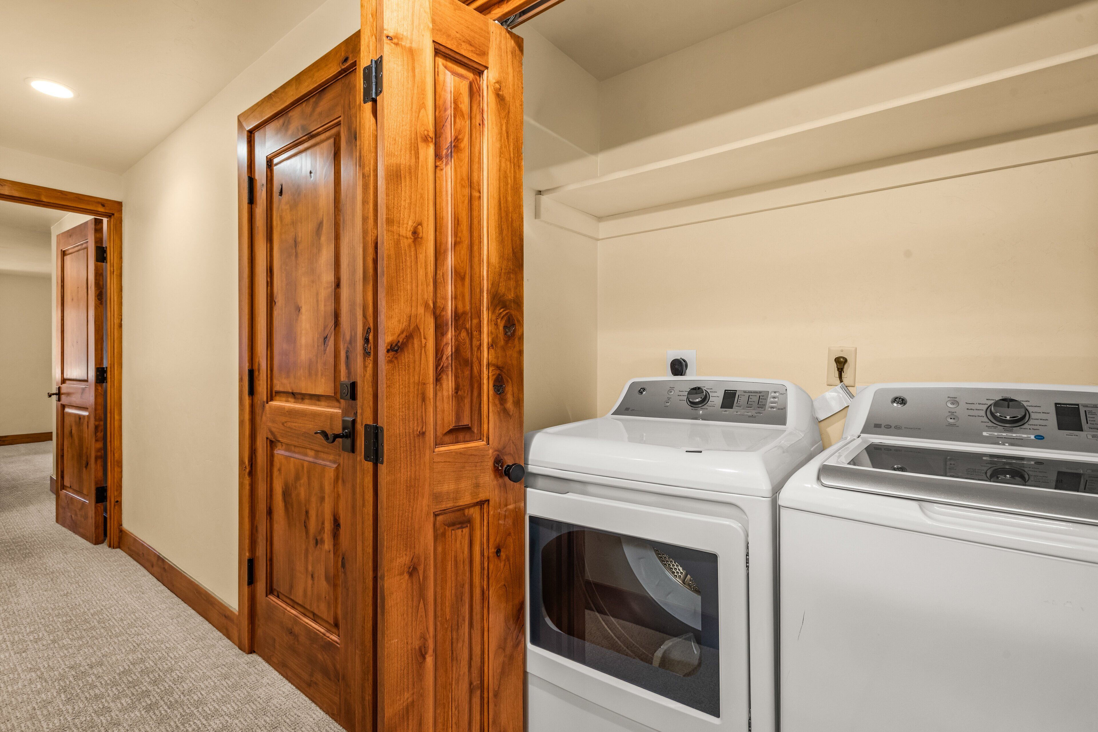 A laundry room with two white front-loading washing machines and a wooden door.