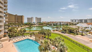 A hotel with a swimming pool, palm trees, and a view of a lake and other buildings. - High-Rise Destin Condo w/ Balcony + Pool View (Destin)