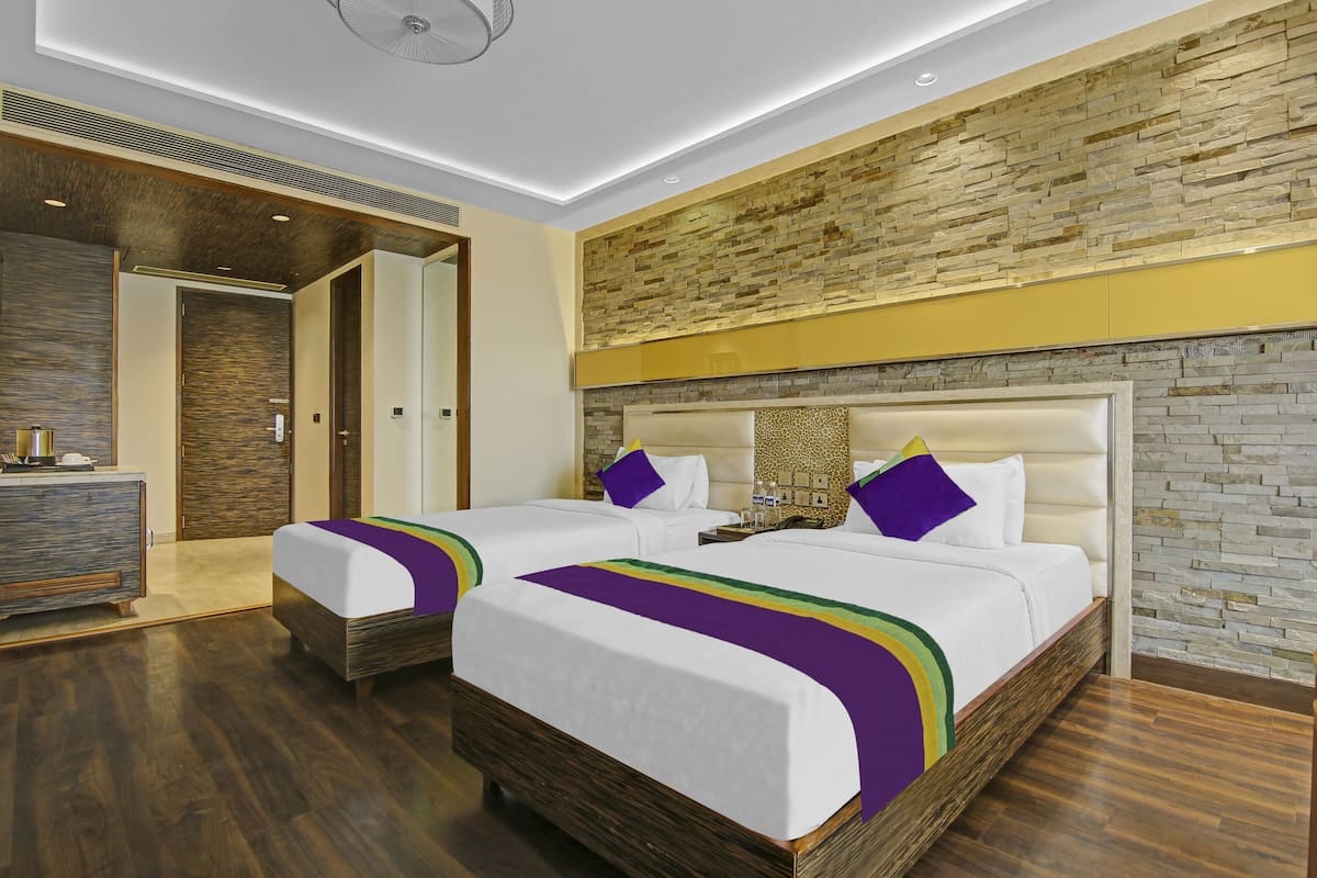 Habitación de hotel con dos camas, suelo de madera, pared de piedra y diseño de techo moderno.