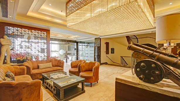 A spacious lobby with a modern chandelier, leather sofas, a glass coffee table, and a large cannon display. - Treebo Premium Arista (Mohali)