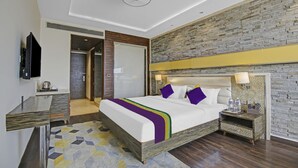 A modern hotel room with a large bed, a flat-screen TV, a desk with a kettle, and a stone-textured wall. - Treebo Premium Arista (Mohali)