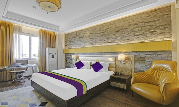 A hotel room with a large bed, a desk, a chair, and a leather armchair. - Treebo Premium Arista (Mohali)
