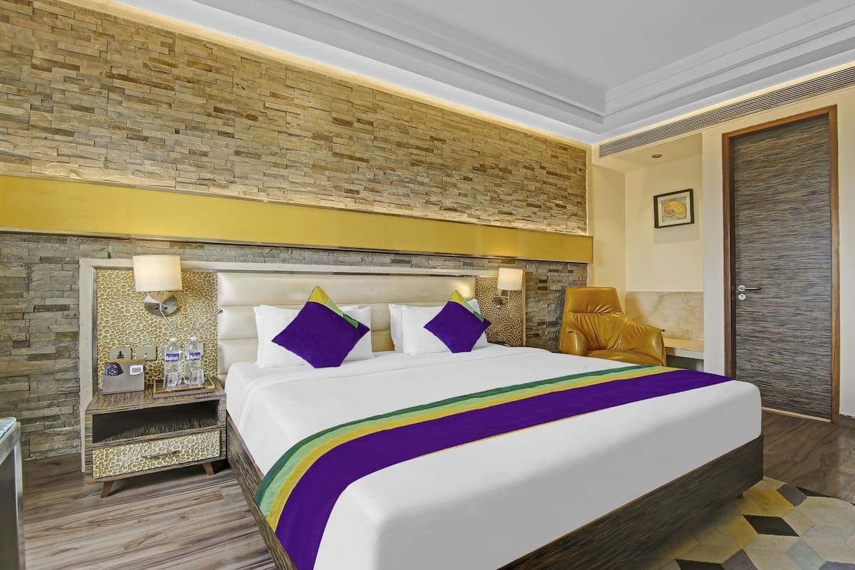 Habitación de hotel con pared de ladrillo, cama con colcha a rayas de arcoíris, mesita de noche con lámpara y puerta con panel texturizado.