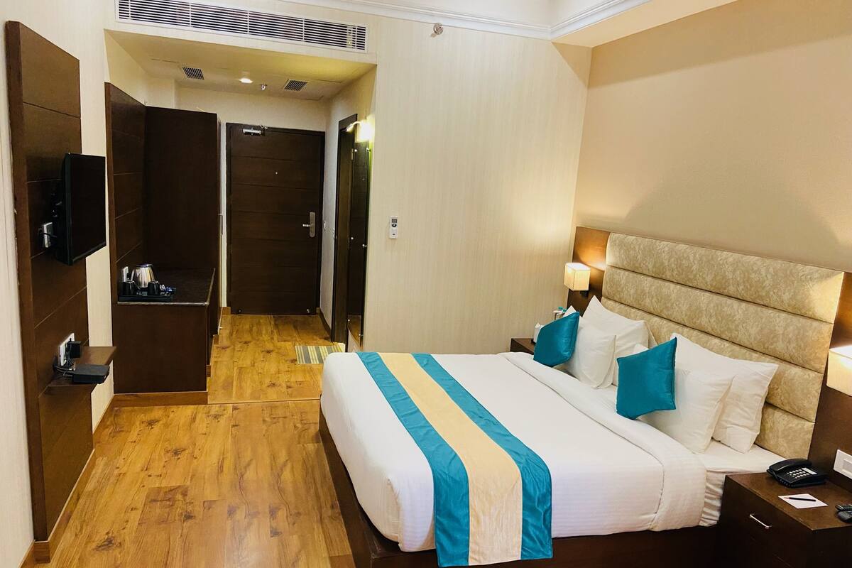 Habitación de hotel con una cama grande, mesitas de noche, televisión y un baño visible a través de una puerta abierta.