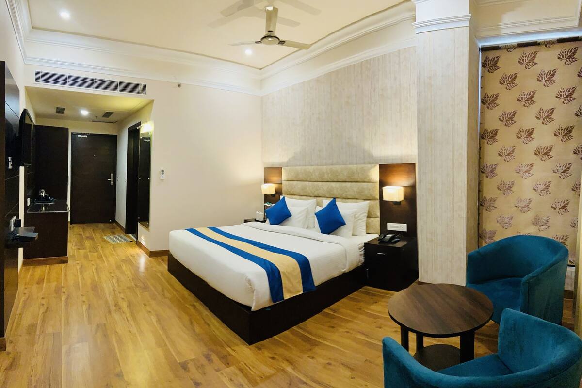 Una habitación de hotel con cama, mesitas de noche, una silla, una pequeña mesa y un ventilador de techo.