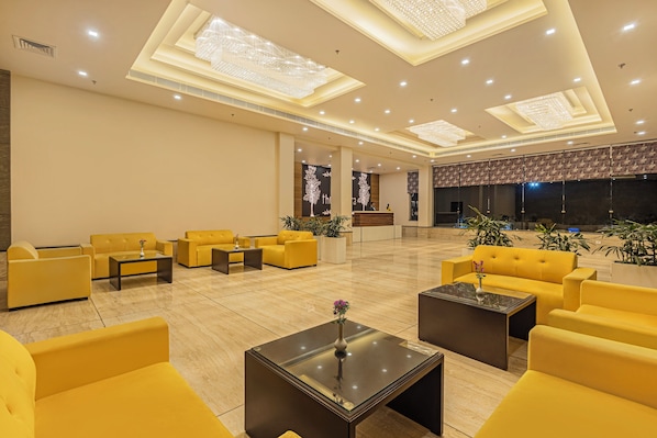 A spacious lobby with yellow sofas, a reception desk, and modern chandeliers.