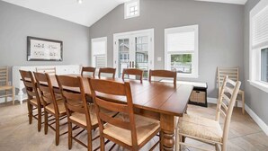 Un comedor con una gran mesa de madera y sillas, un ventilador de techo y una ventana con persianas.