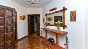 Een hal met houten vloer, een houten deur, een kroonluchter, een console tafel met vazen en kunst aan de muur.