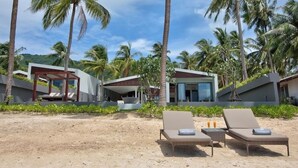 A beachfront property with modern architecture, including a covered outdoor seating area and lounge chairs on the sand. - Beachfront Villa . Private Beach & Pool. 3 bedrooms.  Housekeeper included . (Koh Samui)