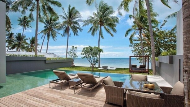 A poolside area with lounge chairs and a table, surrounded by palm trees and a view of the ocean. - Beachfront Villa . Private Beach & Pool. 3 bedrooms.  Housekeeper included . (Koh Samui)