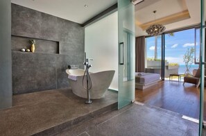 A modern bathroom with a freestanding bathtub, a glass shower enclosure, and a stone wall with decorative items.