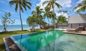A swimming pool with a clear blue water edge, surrounded by palm trees and a view of the ocean.