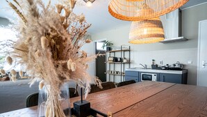 A modern kitchen with a wooden dining table, a vase with dried flowers, and wicker pendant lights. - The Lion King (Groningen)