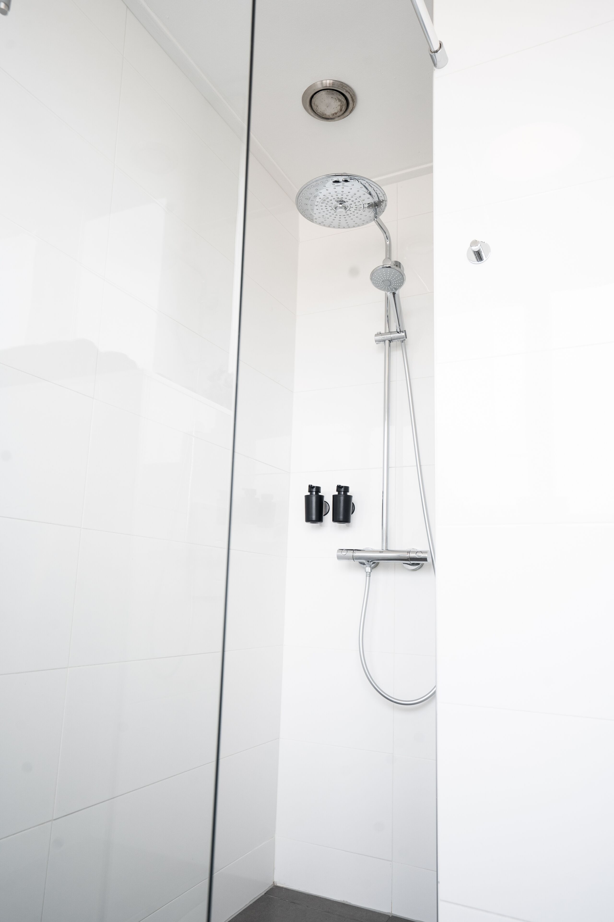 Een moderne douche met een handdouche en een wandmengkraan, voor een witte betegelde muur.