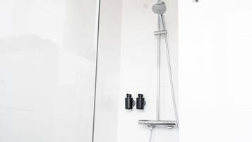 Een moderne douche met een handdouche en een wandmengkraan, voor een witte betegelde muur.
