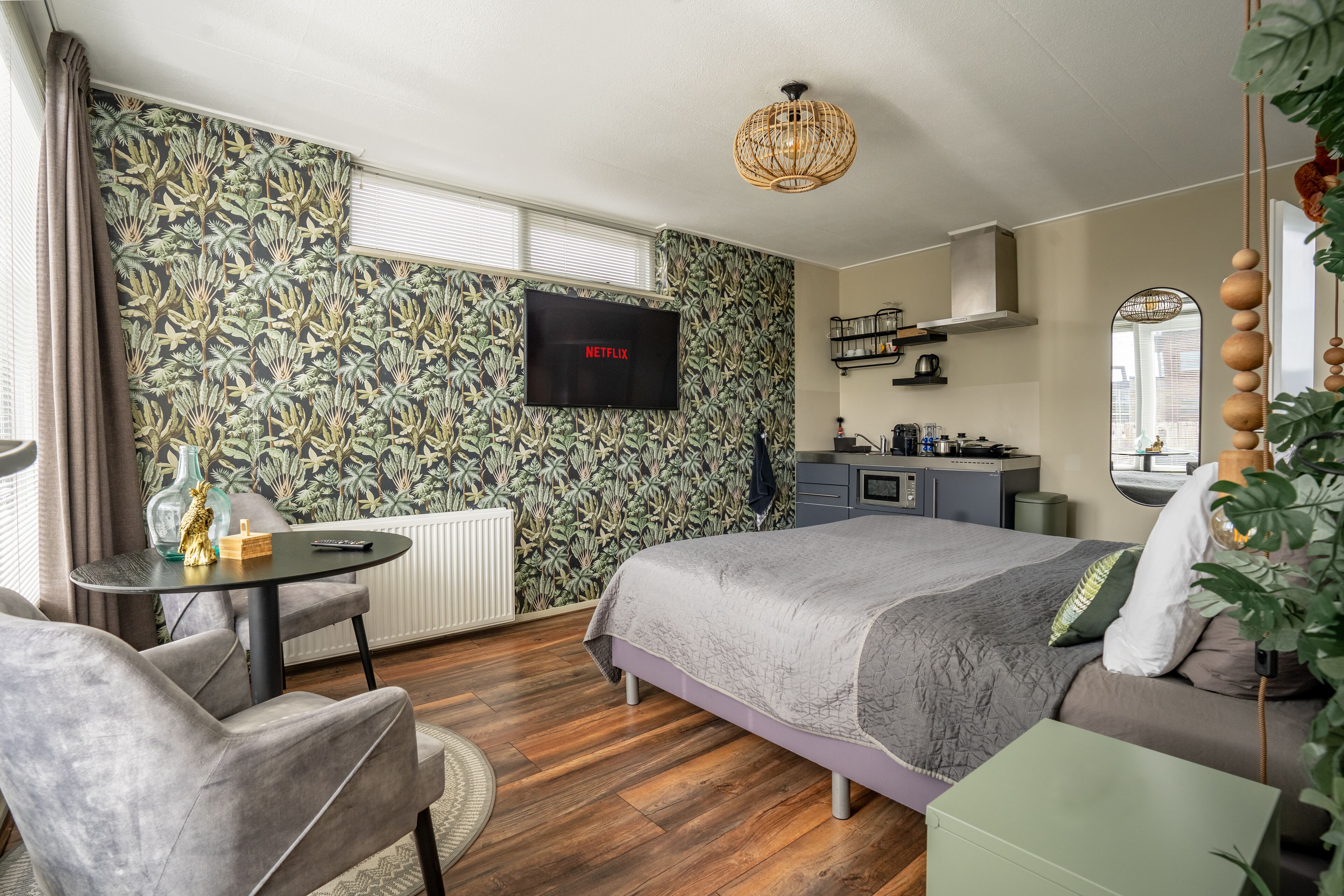 A bedroom with a bed, a desk, a chair, a television, and a kitchen area.