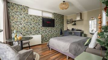 A bedroom with a bed, a desk, a chair, a television, and a kitchen area.