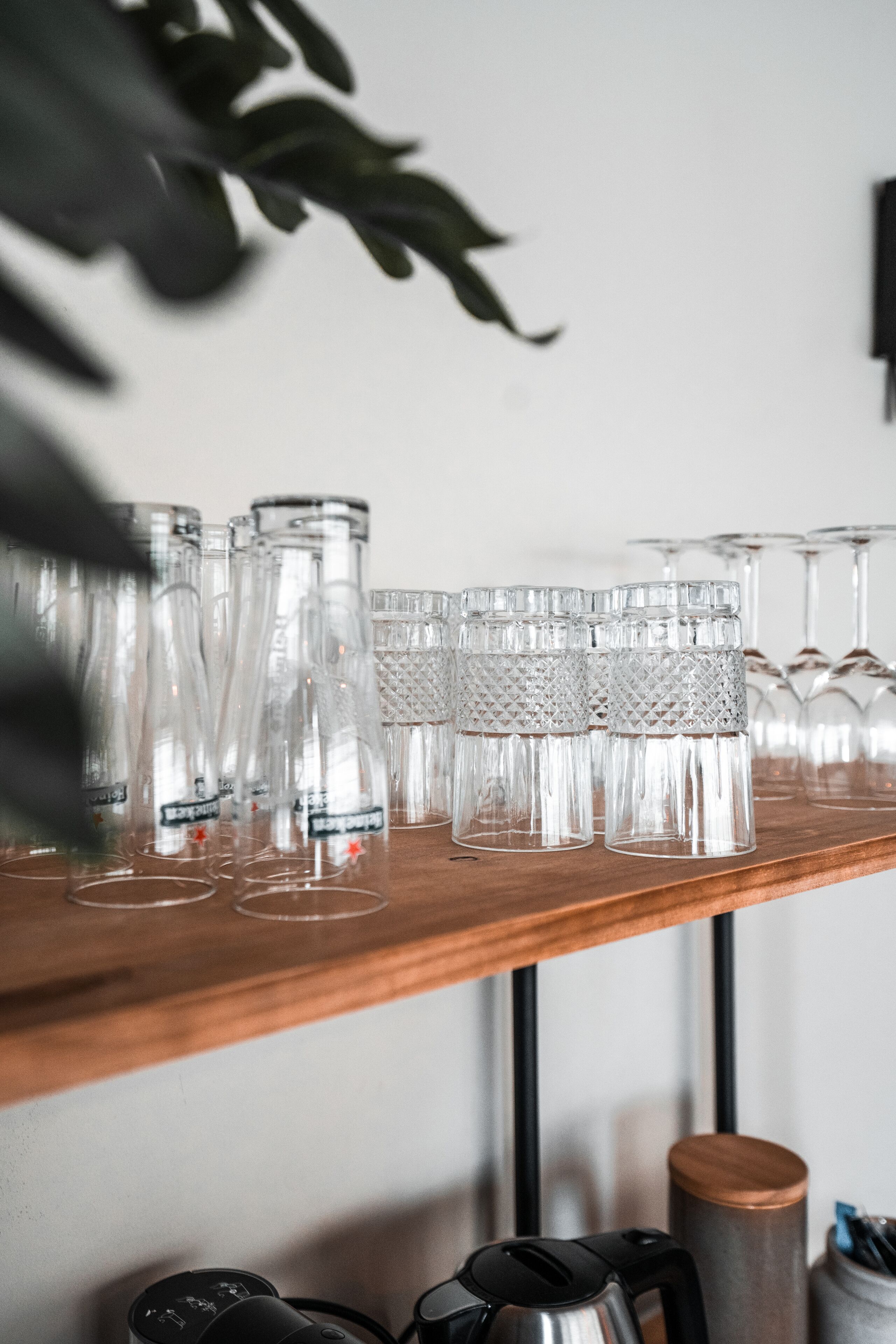 Una estantería de madera con varios vasos de vidrio transparentes y algunos vasos con tallo.