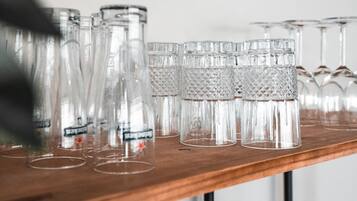 A wooden shelf with multiple clear glass tumblers and a few stemmed glasses.
