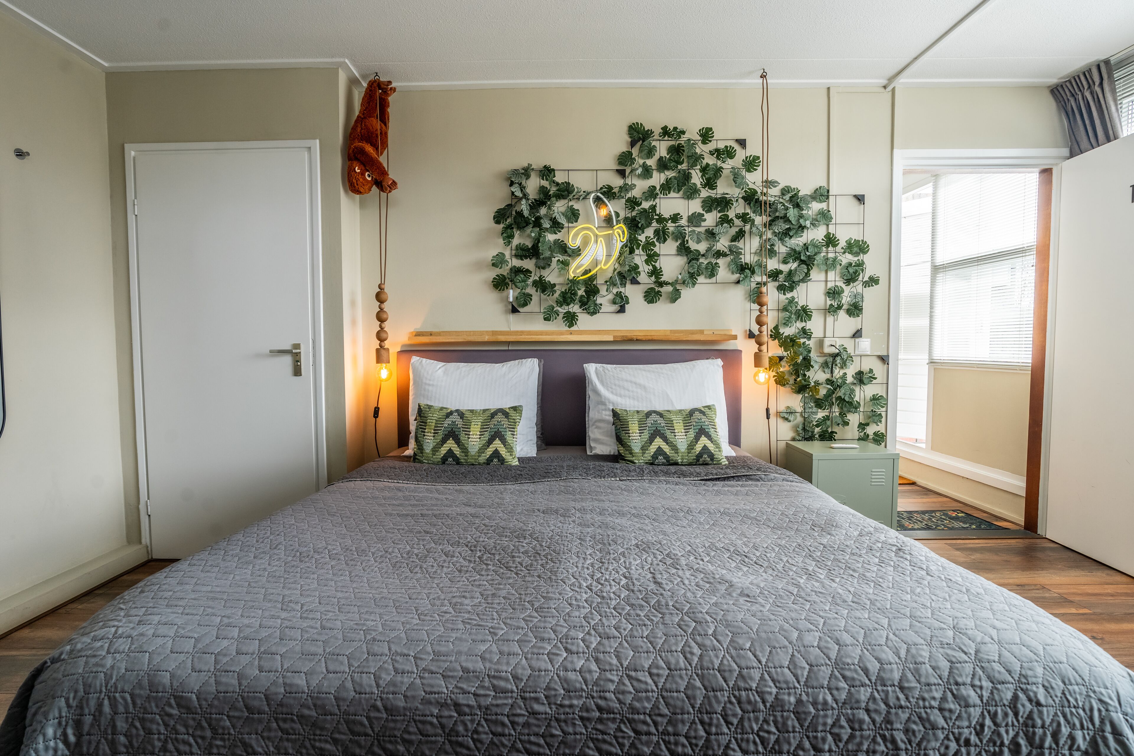 A bedroom with a large bed, two pillows, a headboard, a wall-mounted plant, and a door.