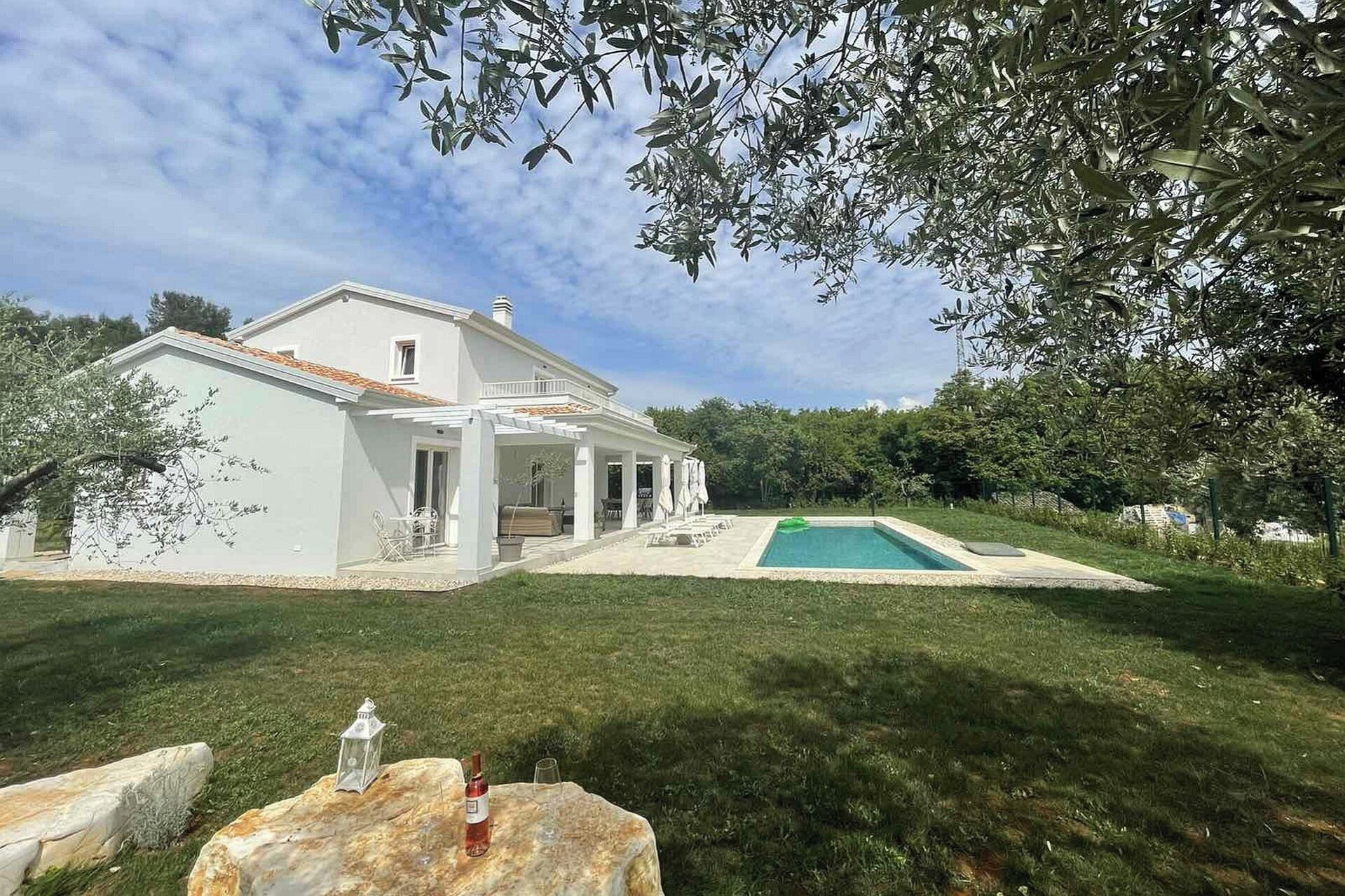 Ein weißes Haus mit Swimmingpool, überdachter Terrasse und Rasen.