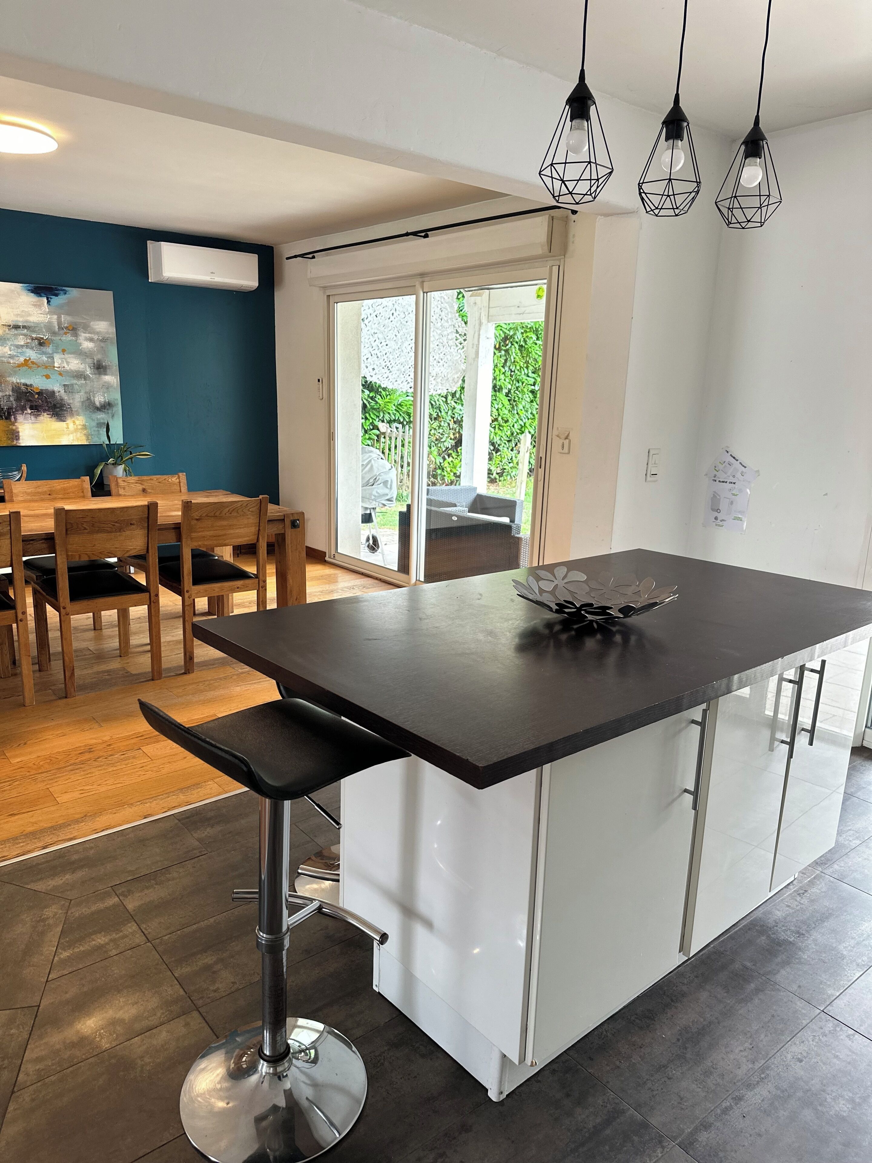 Una cucina moderna con isola centrale, una zona pranzo con sedie in legno e vista su un patio esterno attraverso porte vetrate.