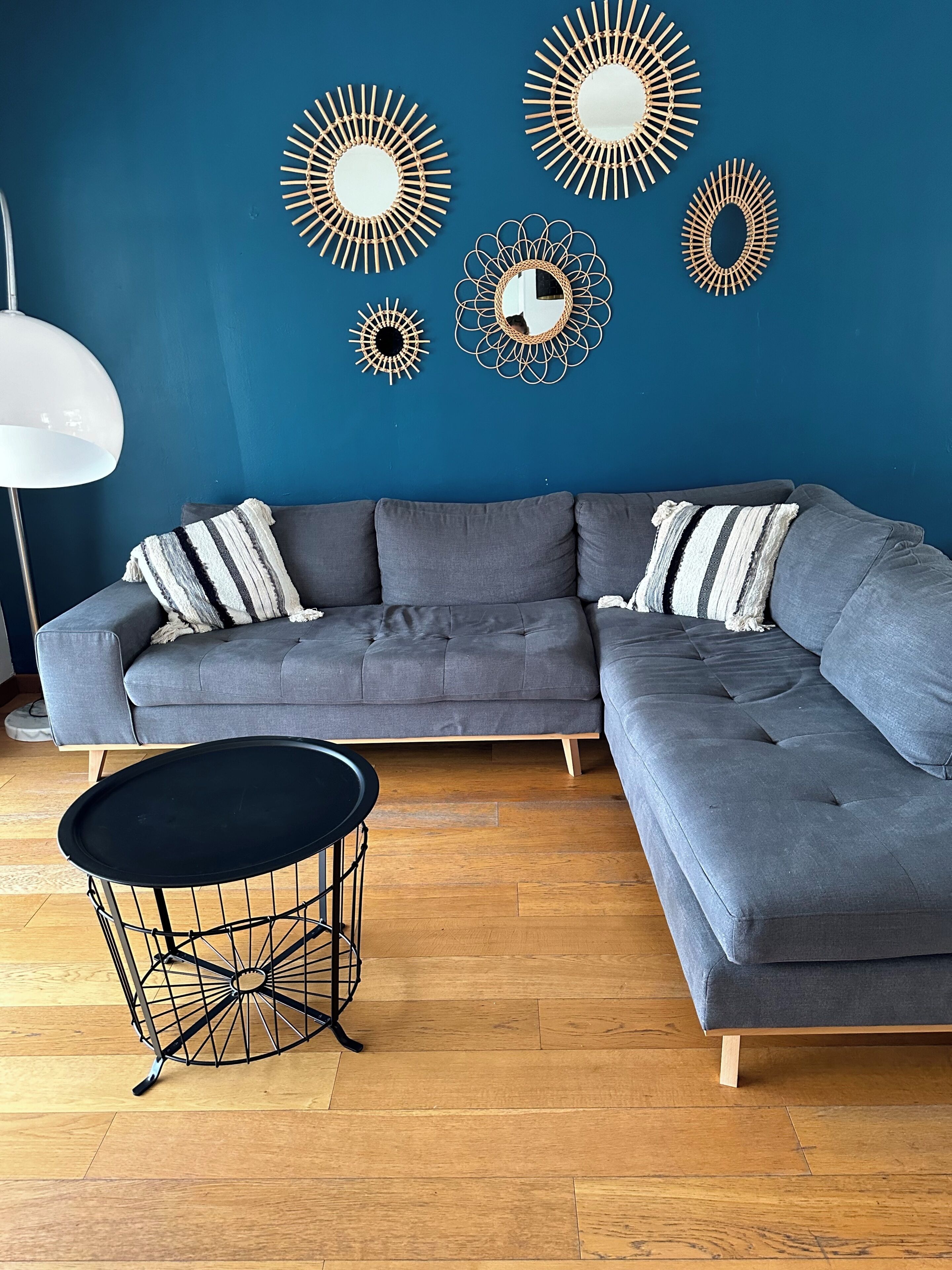 Un soggiorno moderno con un divano angolare grigio, un tavolino da caffè nero rotondo e specchi decorativi a parete.