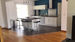 Uma cozinha moderna com armários brancos, uma área de refeições com mesa e cadeiras, e piso de madeira.