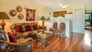 Ein Wohnzimmer mit Korbmöbeln, einem Deckenventilator und einer Küchenzeile mit Holzausbau.