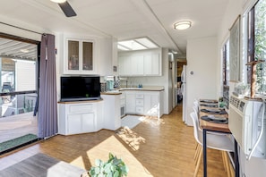 Una cocina moderna con armarios blancos, televisor integrado y un comedor con mesa y sillas de madera.
