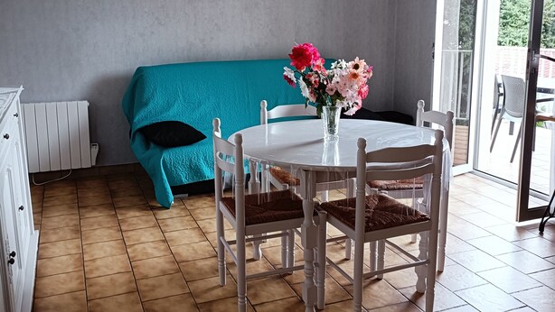 Un coin repas avec une table et des chaises blanches, un canapé de couleur turquoise et un vase à fleurs.