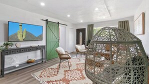 A modern living room with a large flat-screen TV, a green sliding door, a wicker hanging chair, and a decorative rug. - Modern Family Home | Rooftop Patio | Game Room (Denver)