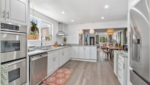 A modern kitchen with stainless steel appliances, white cabinetry, and a central island. - Modern Family Home | Rooftop Patio | Game Room (Denver)