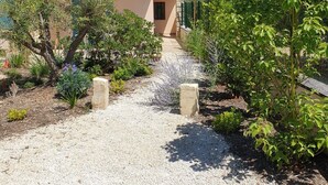 A house with a tiled roof, a gravel pathway leading to the entrance, and various plants and shrubs around. - Charming cottage in Saint Remy de Provence, 4-5 people with pool and garden (France)