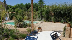 An outdoor patio with a round table and chairs, surrounded by greenery and a swimming pool. - Charming cottage in Saint Remy de Provence, 4-5 people with pool and garden (France)
