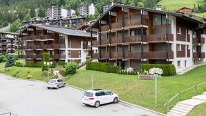 Ein mehrstöckiges Hotel mit Balkonen, einem Parkplatz und einer Bergkulisse.