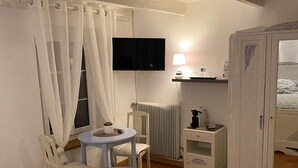 Une chambre à coucher comprenant un lit, une télévision, une petite table avec une chaise, une armoire et un radiateur.